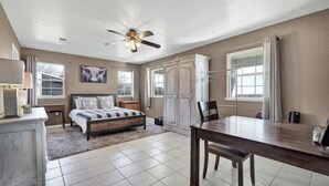 A bedroom with a bed, bedside tables, a desk, a chair, a ceiling fan, and a window. - Casa Blanca: Hot-Tub & Firepit w/Hill Country View (Fredericksburg)