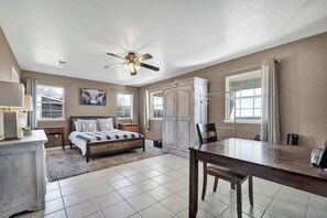 A bedroom with a bed, bedside tables, a desk, a chair, a ceiling fan, and a window. - Casa Blanca: Hot-Tub & Firepit w/Hill Country View (Fredericksburg)