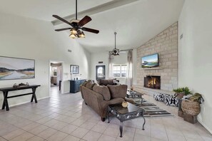 A spacious living room with a fireplace, a ceiling fan, and a television mounted on the wall.