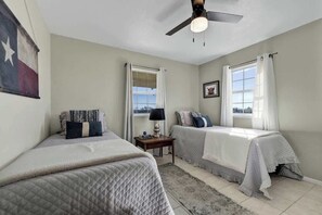 Un dormitorio con dos camas, ventilador de techo y una ventana con cortinas.