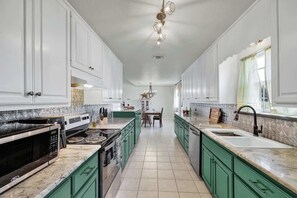 A spacious kitchen with white cabinets, green countertops, and a central island.