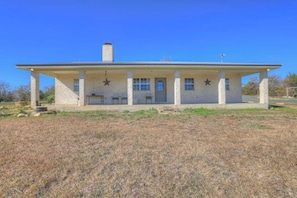 A two-story building with a flat roof, a chimney, and a covered porch with four chairs. - Casa Blanca: Hot-Tub & Firepit w/Hill Country View (Fredericksburg)
