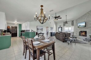 Amplia sala de estar con chimenea, una mesa de comedor con sillas y una cocina al fondo.