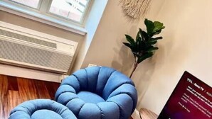 A room with a wooden floor, a blue cushioned seating area, a plant, a wall-mounted macrame piece, and a TV on a wooden stand. - 503 Bohemian Romance Apartments in center city (Philadelphia)