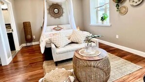 A bedroom with a canopy bed, a round wooden side table, and a woven pouf. - 503 Bohemian Romance Apartments in center city (Philadelphia)