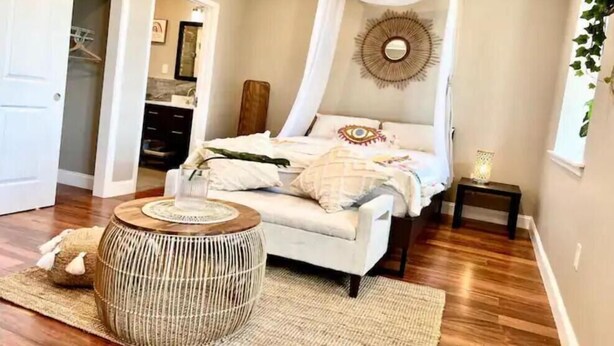 A bedroom with a canopy bed, a bedside table, a round wooden stool, and a mirror on the wall. - 503 Bohemian Romance Apartments in center city (Philadelphia)