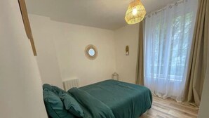 Quarto com cama, radiador, janela com cortinas e luminária suspensa.