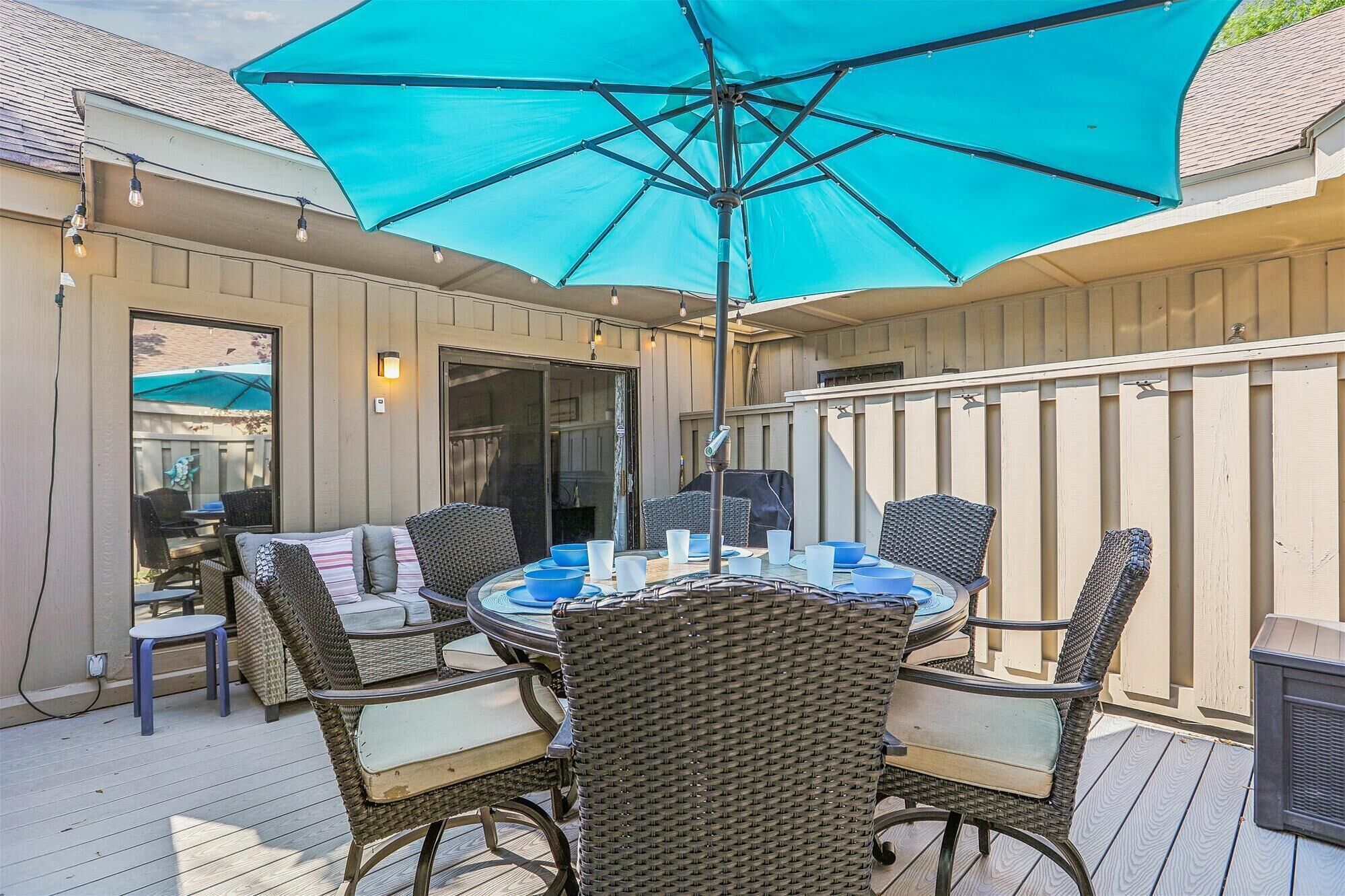 A covered patio with a round table and wicker chairs, a blue umbrella, and a sliding glass door.
