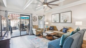 Un salon spacieux doté d’un ventilateur de plafond, d’une grande fenêtre offrant une vue sur l’extérieur, d’un coin repas avec une table et des chaises, et d’un canapé agrémenté de coussins décoratifs.