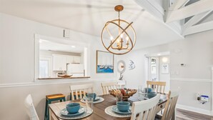 Un coin repas avec une table en bois, des chaises blanches et un lustre.