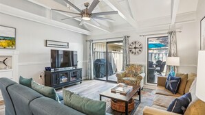 Un salon spacieux doté d’un ventilateur de plafond, d’un téléviseur à écran plat, d’un canapé, d’une table basse et d’une vue sur une terrasse extérieure, accessible par une porte-fenêtre coulissante.