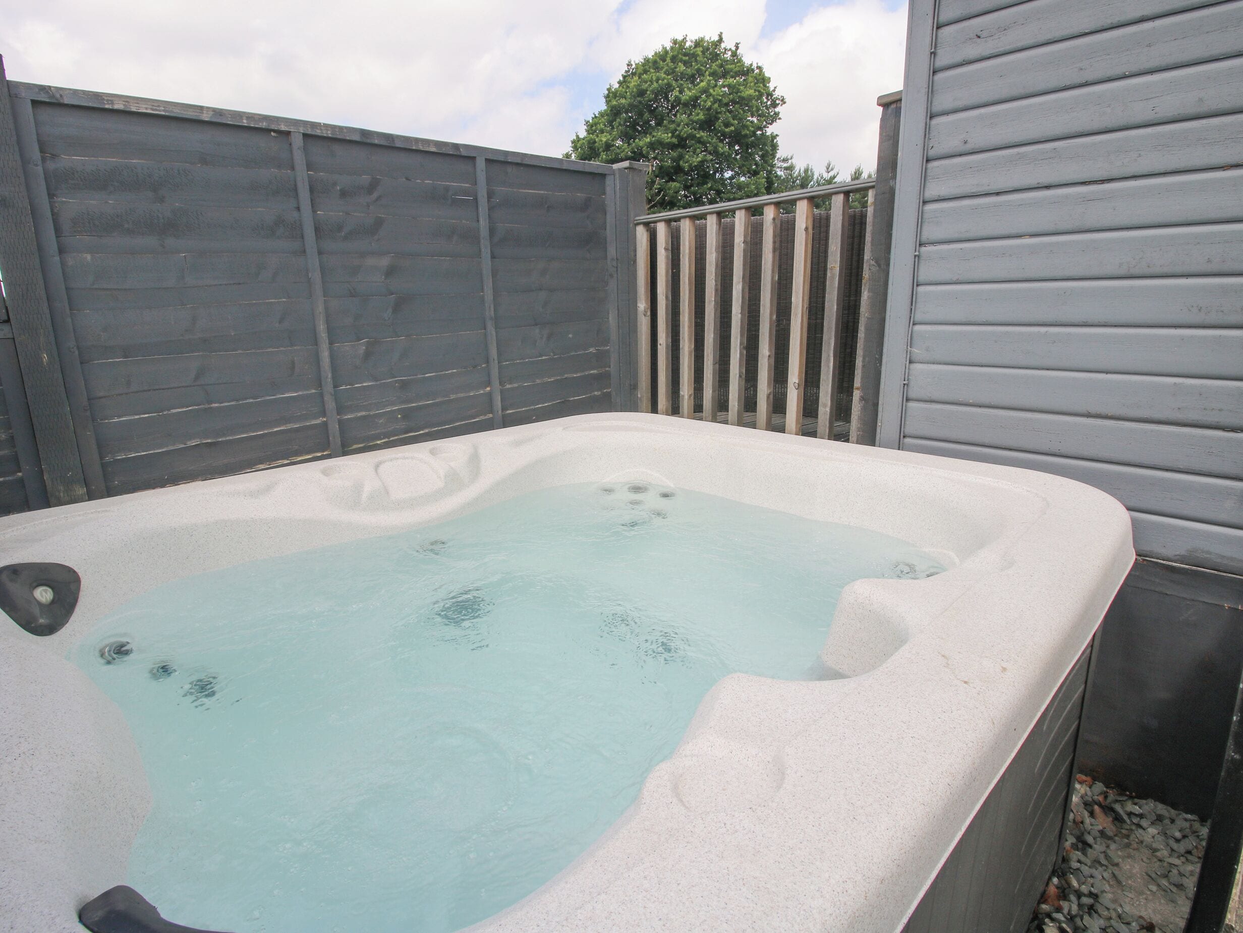 A hot tub in an outdoor setting with a wooden fence and a house in the background.
