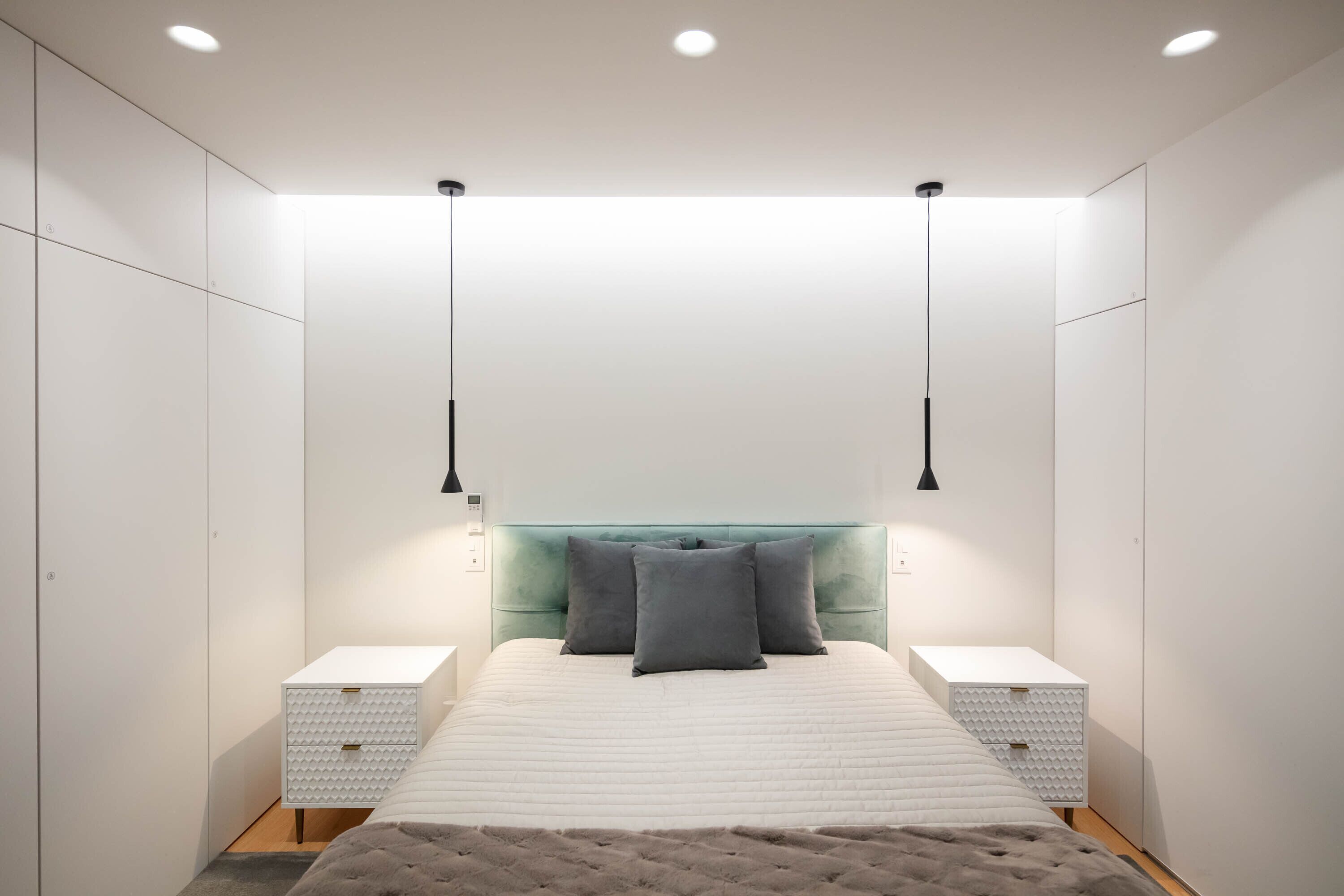 A modern bedroom with a large bed, two bedside tables, a teal headboard, and pendant lights.