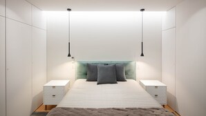 A modern bedroom with a large bed, two bedside tables, a teal headboard, and pendant lights.