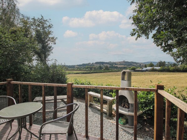 An outdoor patio with a table and chairs, a stone fireplace, and a view of a rural landscape. - Aston - Shepherd Hut (Craven Arms)