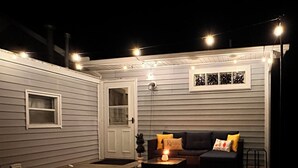 Une terrasse extérieure accueillante, dotée d’un foyer, d’un canapé avec des coussins et de guirlandes lumineuses.