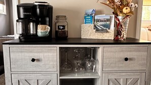 Un meuble en bois contenant une machine à café, une tasse, un bocal, un livre et un vase avec des fleurs séchées.