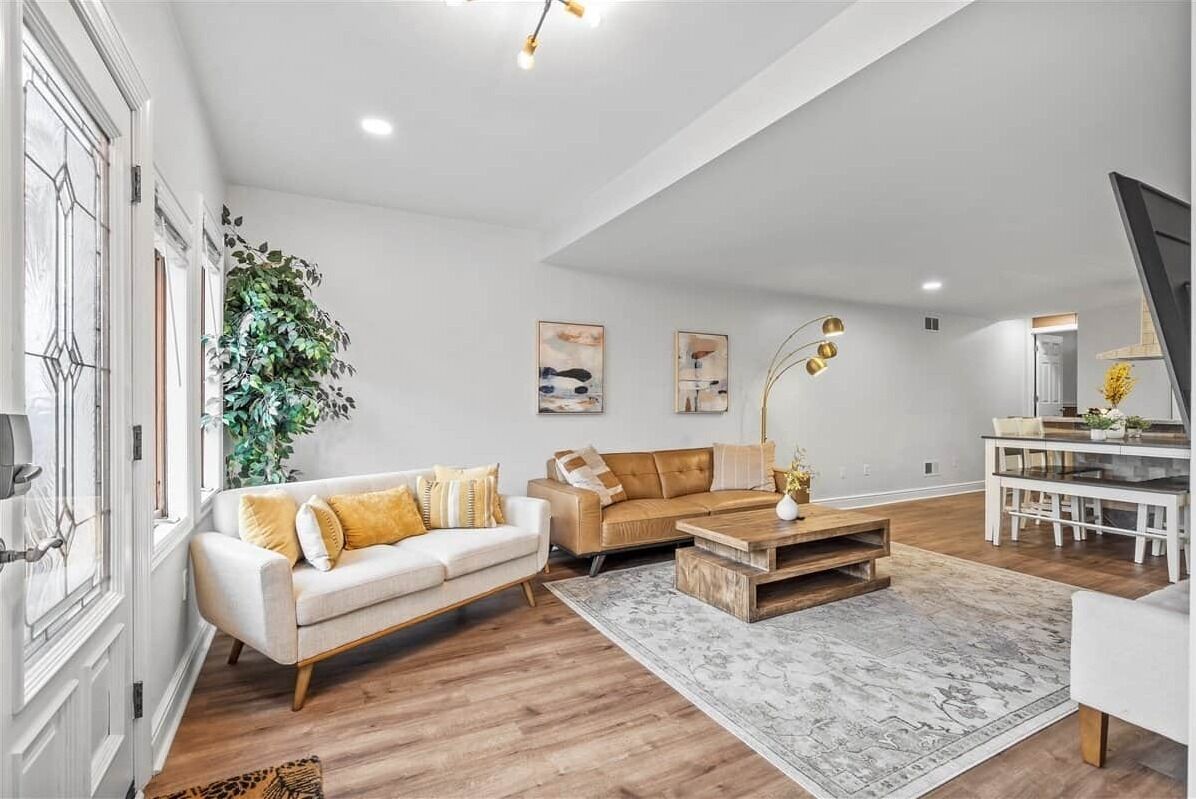 Een ruime woonkamer met een witte bank, een bruine leren bank, een houten salontafel en een eethoek met een glazen tafel.
