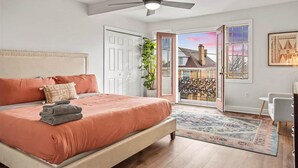 A bedroom with a bed, a ceiling fan, a door leading to a balcony, and a view of a house. - Fine View | Rooftop Deck | 4BR (Pittsburgh)