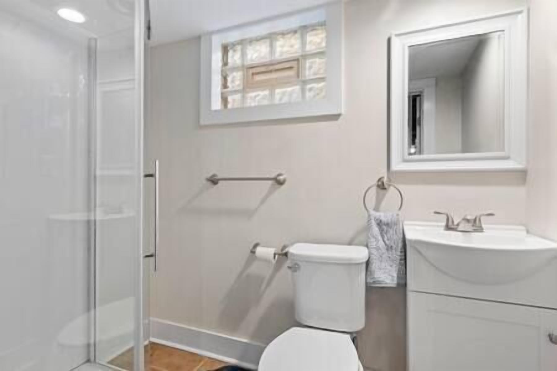 A bathroom with a glass shower enclosure, a toilet, a sink, and a mirror.