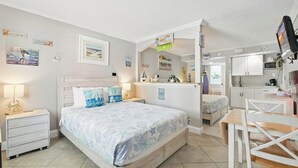 A bedroom with a bed, bedside tables, a desk, and a kitchenette. - Pelican Pointe 111:Walk to Beach~Pool~Free Parking (Clearwater Beach)