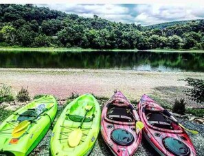 Three kayaks lined up on a gravel shore by a calm lake with dense forest in the background.