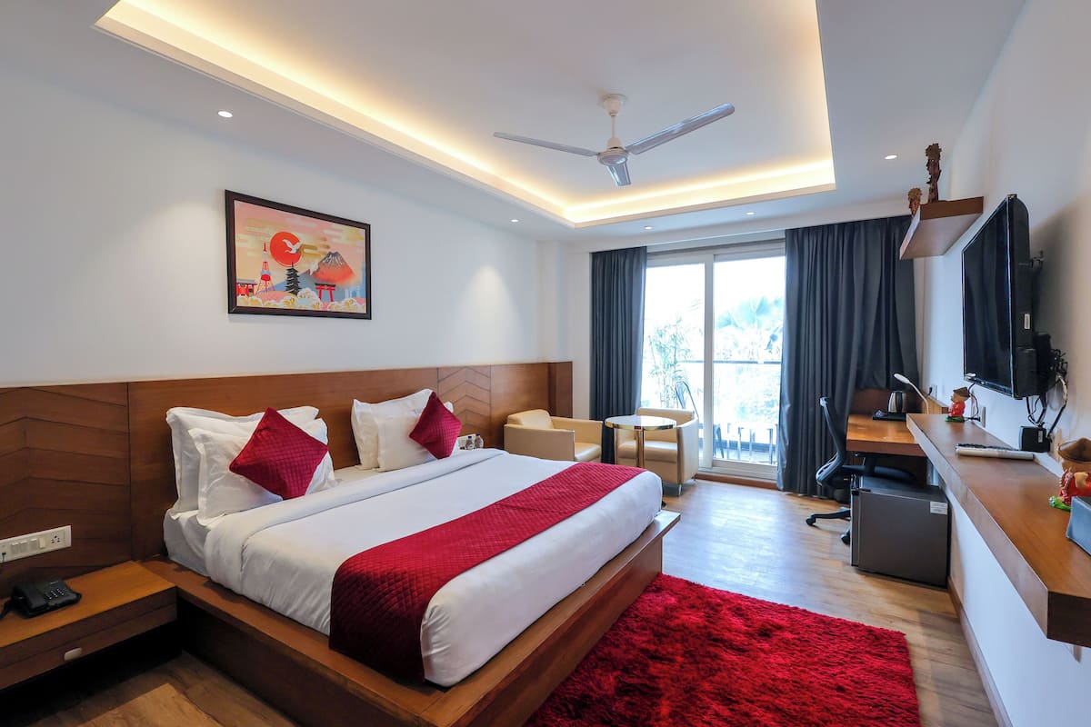 A modern hotel room with a large bed, a desk, a chair, a TV, and a ceiling fan.