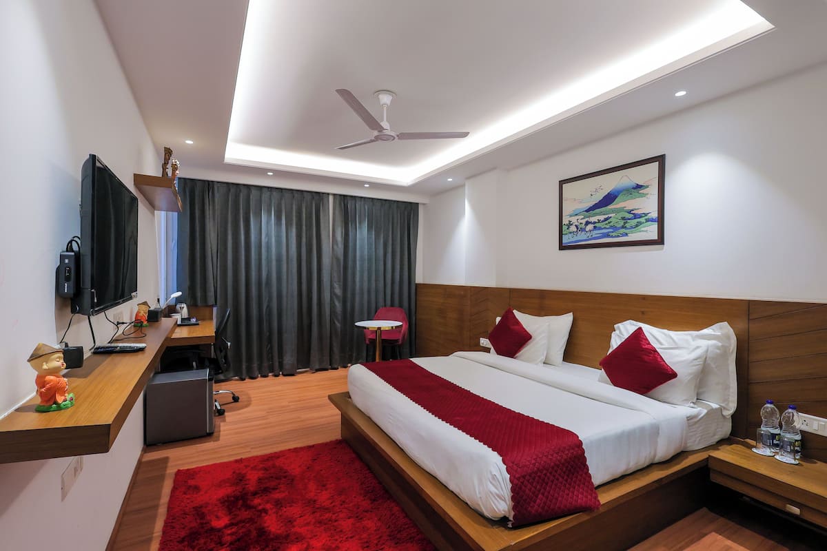 A modern hotel room with a bed, a desk, a chair, a TV, and a painting on the wall.
