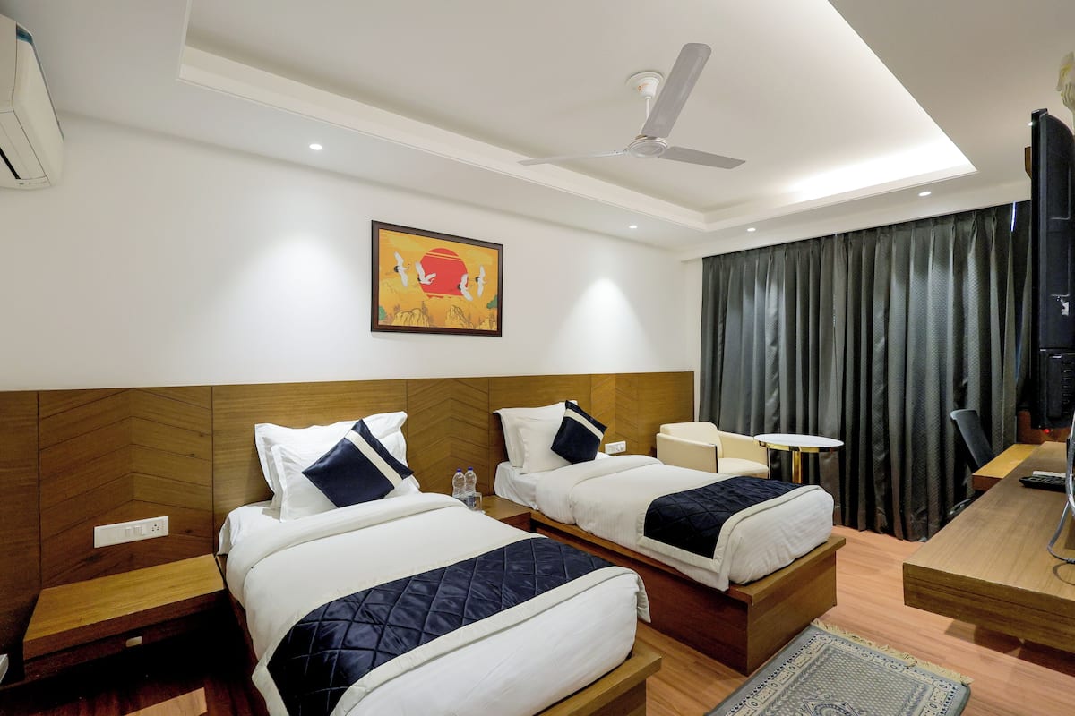 A hotel room with two beds, a ceiling fan, a painting, a TV, and a desk with a chair.