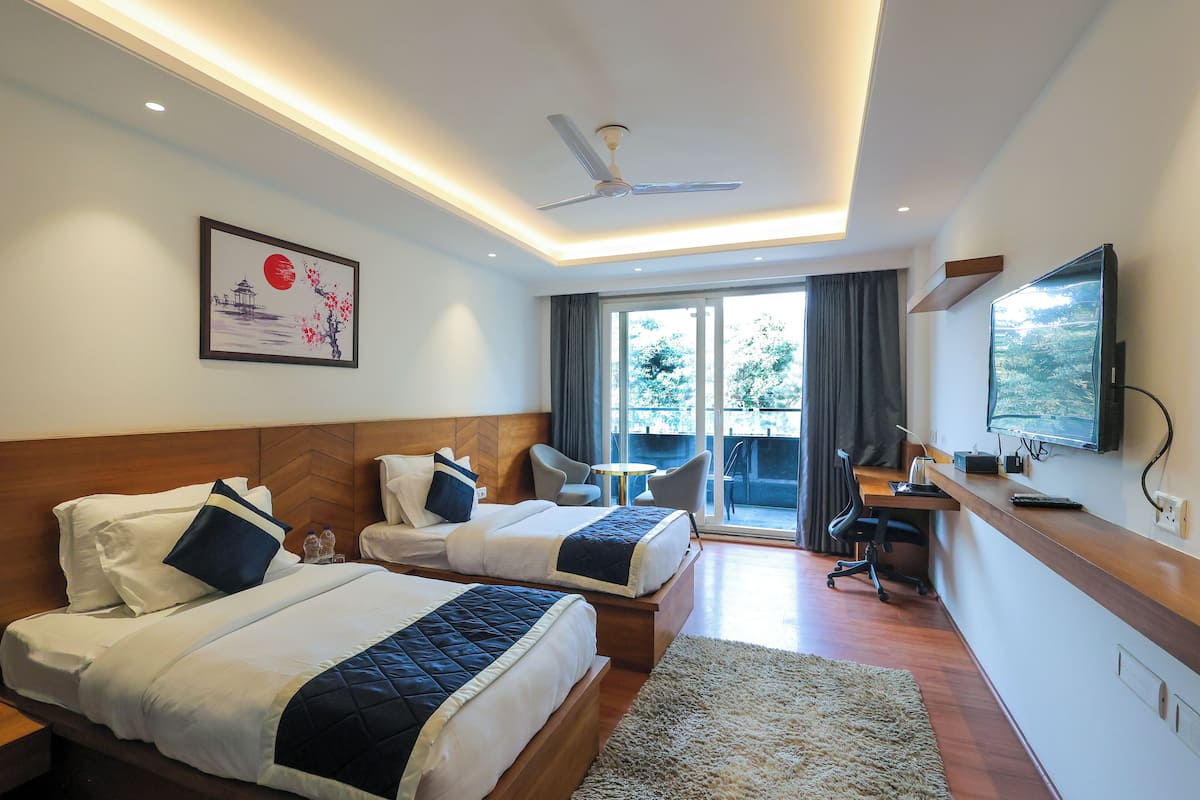 A hotel room with two beds, a desk, a chair, a TV, and a balcony with a view.