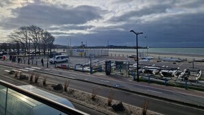 Een kustweg met geparkeerde voertuigen en een jachthaven met boten.