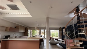 Una cocina moderna con una isla central, una zona de comedor con una mesa grande y una escalera de caracol.