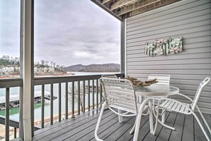 Eine überdachte Terrasse mit Tisch und Stühlen, mit Blick auf ein Gewässer und eine hügelige Landschaft.