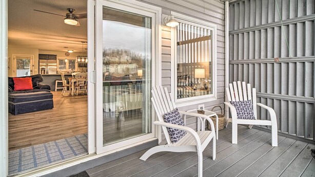 A covered porch with two white Adirondack chairs, a dining table, and a sliding glass door leading to an interior space with a kitchen and dining area. - Deerfield Lakefront Condo/Boat Slip Included! (LaFollette)