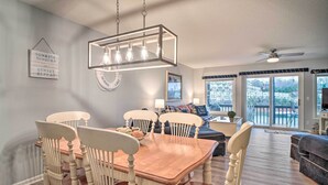 A dining area with a wooden table and chairs, a hanging light fixture, and a view of a balcony with a railing. - Deerfield Lakefront Condo/Boat Slip Included! (LaFollette)