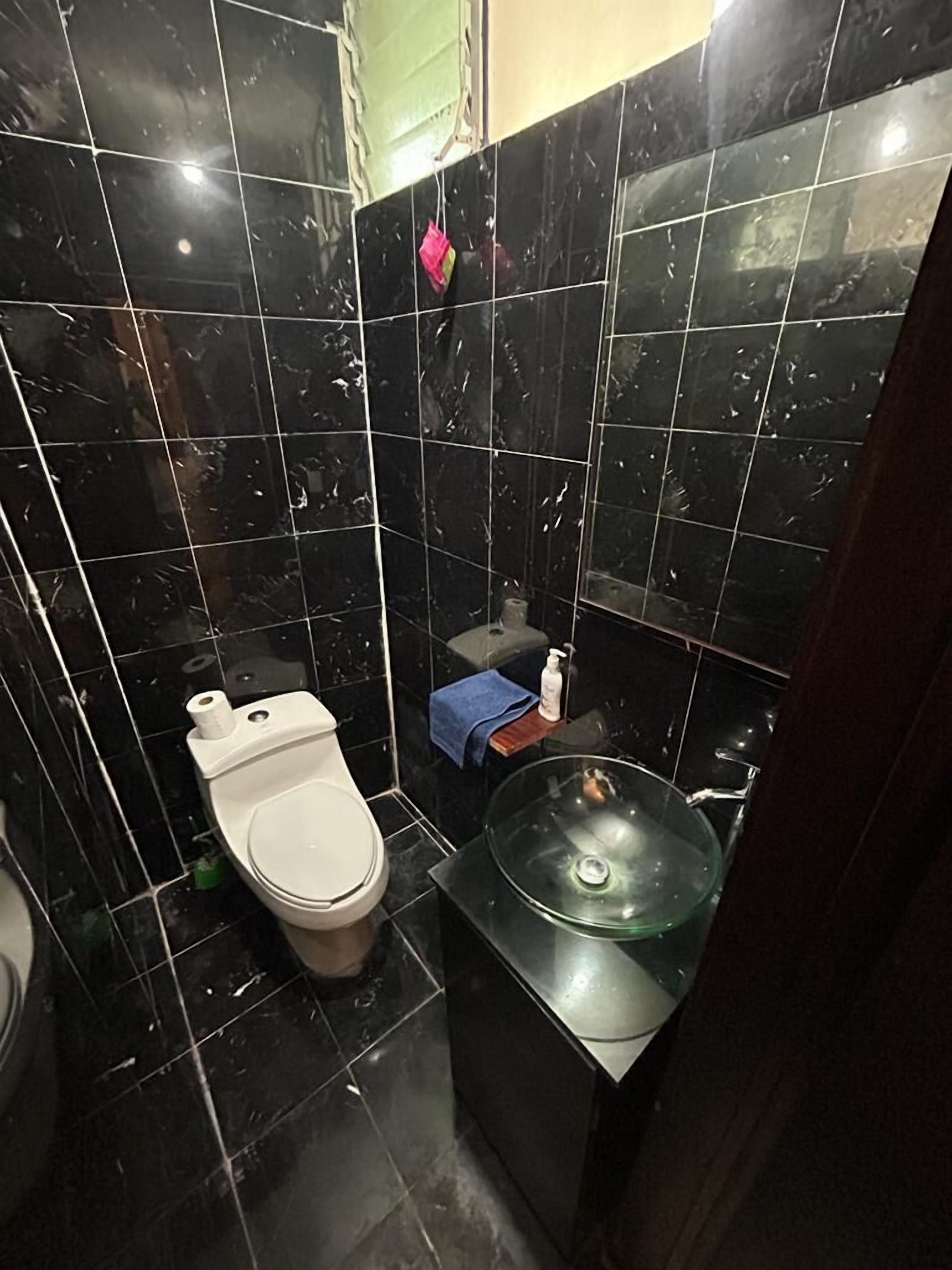 Un baño con baldosas de mármol negro, un inodoro, un lavamanos de vidrio y una toalla azul.