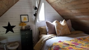 Una camera da letto accogliente in soffitta, con soffitto spiovente, un letto con una coperta colorata, una cassettiera, una decorazione a stella e una finestra con tende.