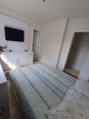 Ett sovrum med en säng, en tv som är monterad på väggen, en garderob och en dörr som leder till ett annat rum.