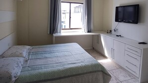 Ein Schlafzimmer mit Bett, Fernseher, Fenster mit Vorhängen, Deckenventilator und Klimaanlage.