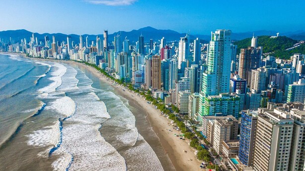 Eine Küstenstadt mit Hochhäusern, einem Strand und Bergen im Hintergrund.
