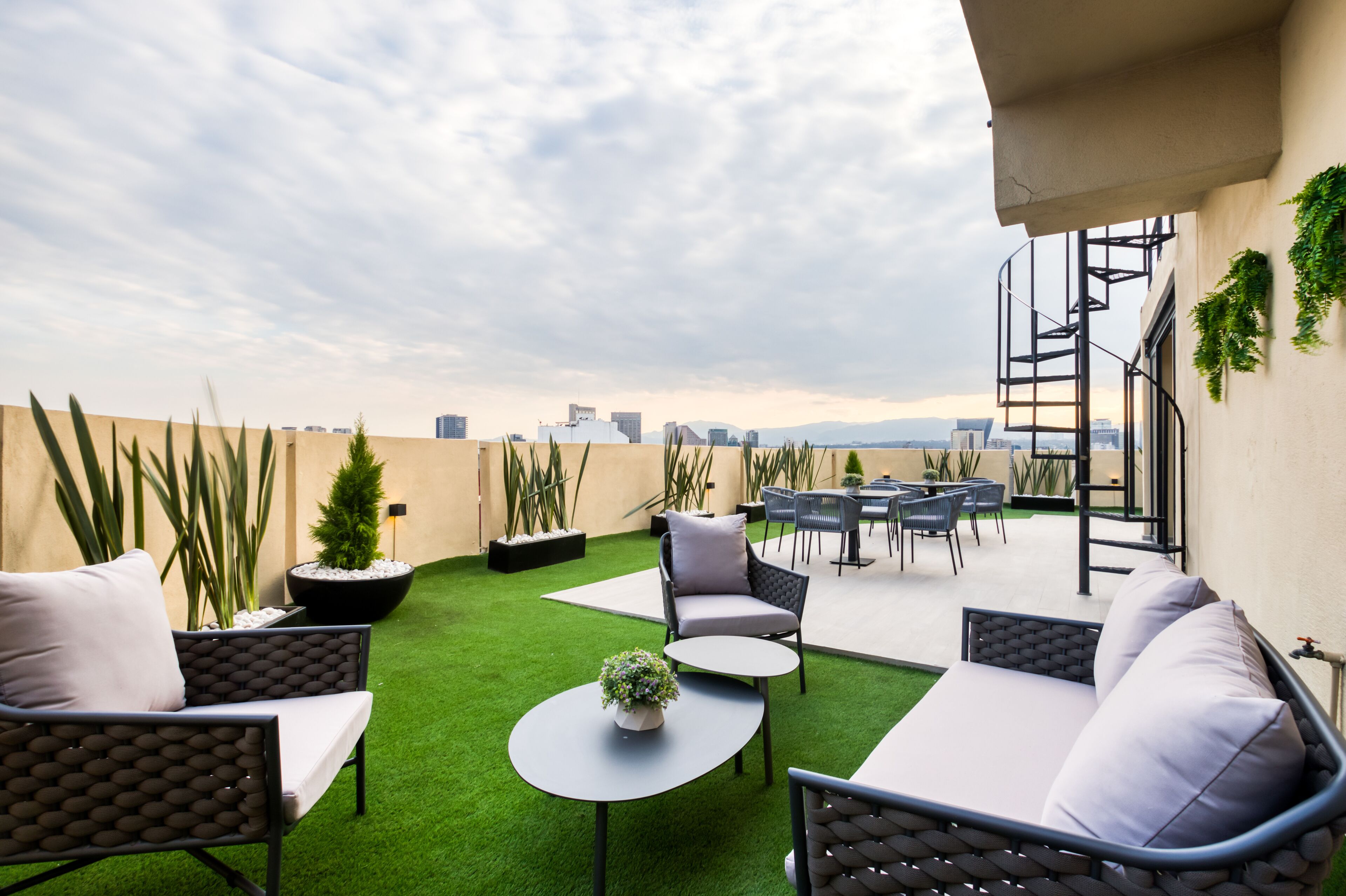 A rooftop patio with outdoor furniture, a small garden area, and a city view.