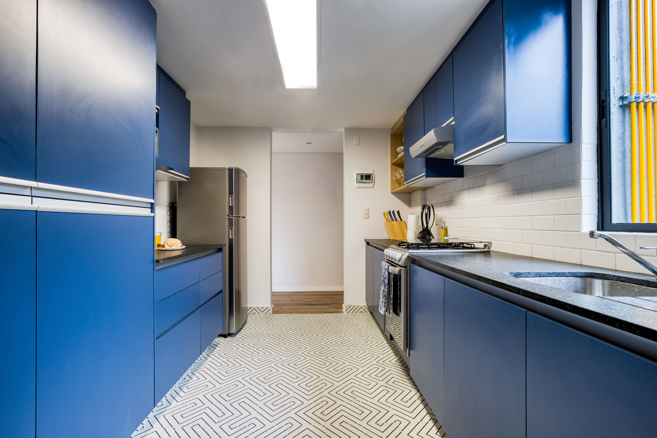 Une cuisine moderne avec des meubles de couleur bleue, un réfrigérateur en acier inoxydable et un plan de travail noir.