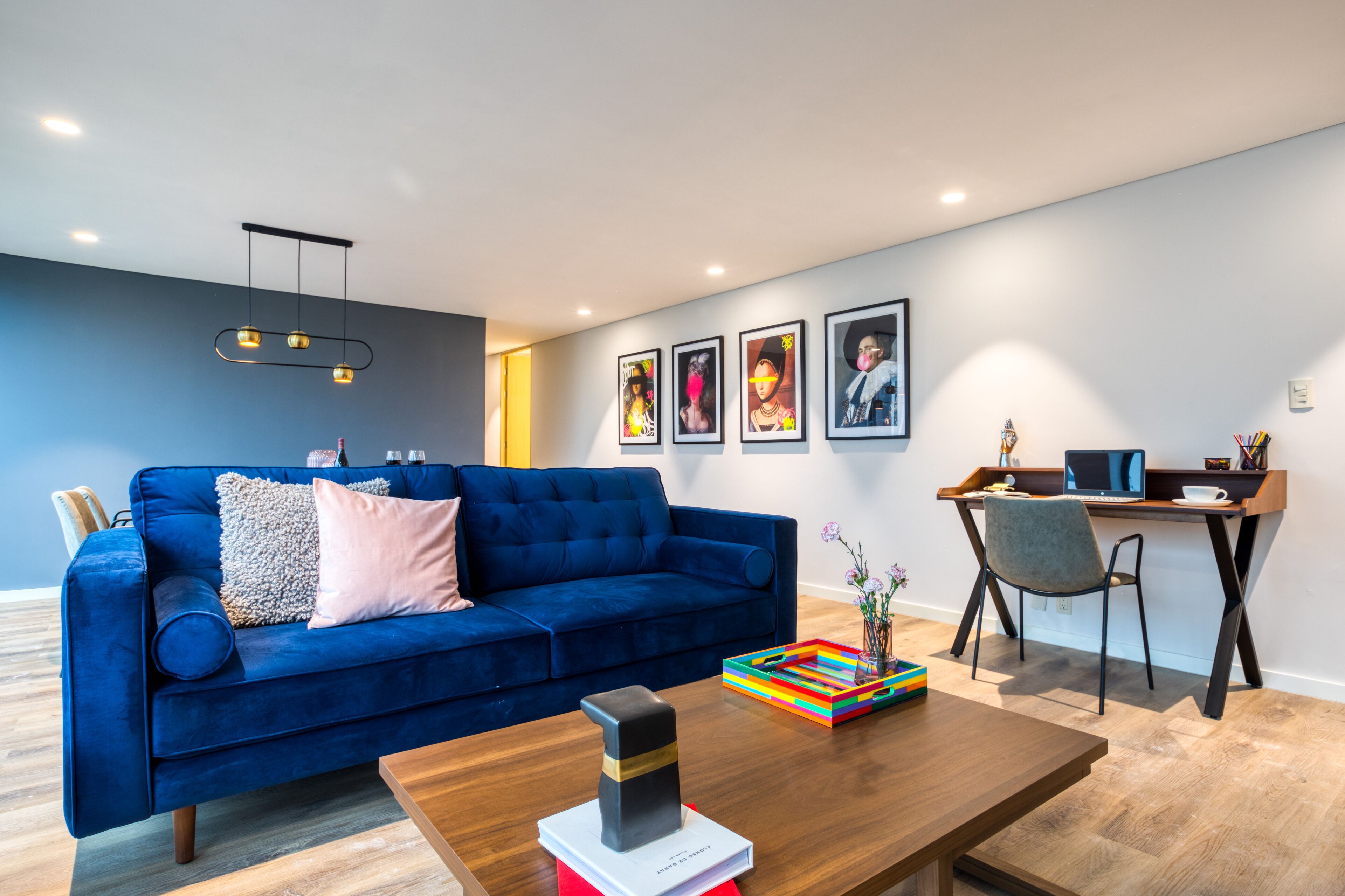 Ein modernes Wohnzimmer mit einem blauen Sofa, einem Holztisch und einem Schreibtisch mit einem Computer.