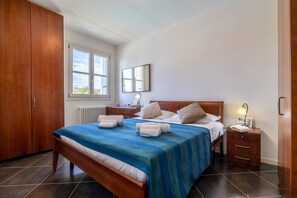 A bedroom with a large bed, wooden wardrobe, bedside tables, and a window with a view. - Corte Fasanella 25 (Toscolano-Maderno)