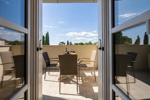 An open glass door leading to a balcony with wicker furniture, a table with glasses, and a view of trees and a clear sky. - Corte Fasanella 25 (Toscolano-Maderno)