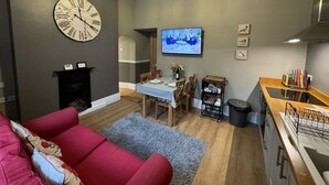 A living room with a red sofa, a wooden dining table with chairs, a TV, and a chandelier. - Cosy self catering apartment in large Victorian Residence (Buxton)