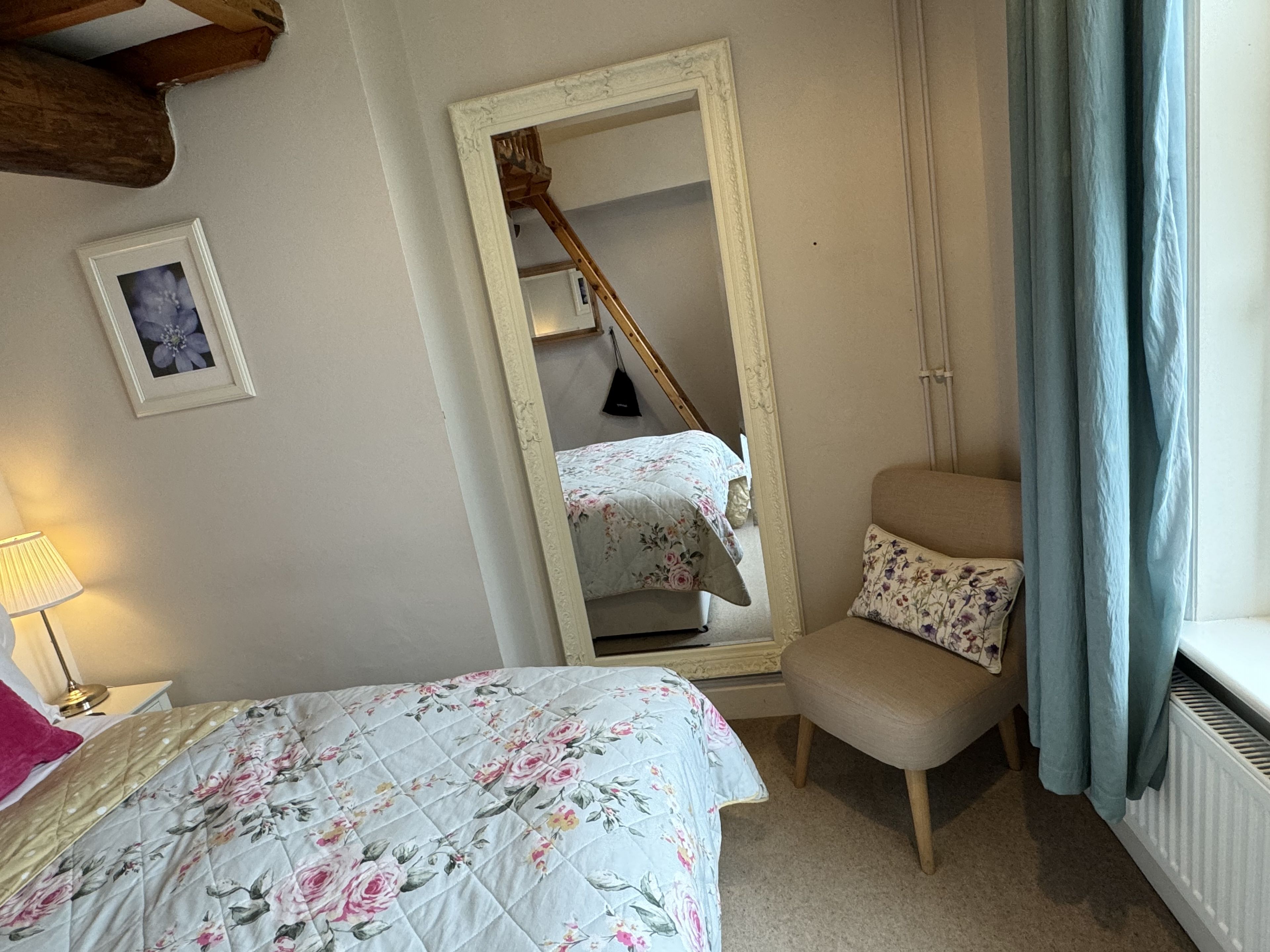 A bedroom with a bed, a chair, a mirror, a picture on the wall, and a window with curtains.