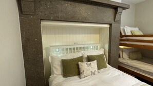 Een slaapkamer met een stapelbed, een wit hoofdeinde en een wand met steenaccenten.