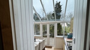 Un invernadero con zona de comedor, cocina y vistas al jardín.
