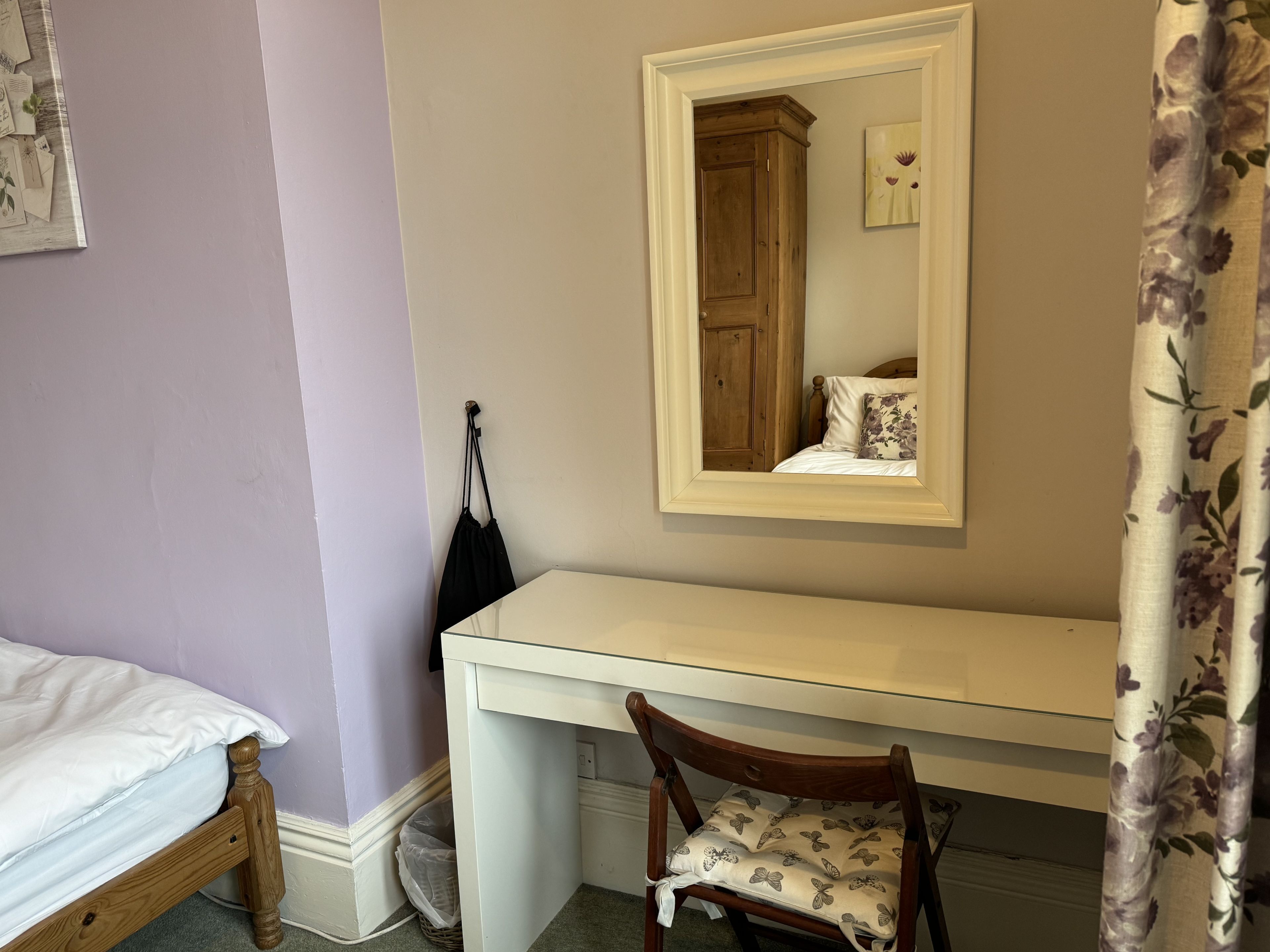 A bedroom with a bed, a desk, a chair, a mirror, and a door.